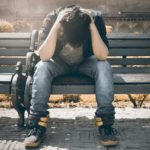 man in black shirt and gray denim pants sitting on gray padded bench