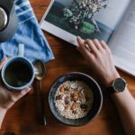 person holding white ceramic coffee cup leaning on brown wooden table