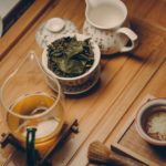 white ceramic teapot beside cup with leaves