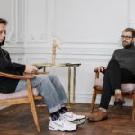 man in black sweater and blue denim jeans sitting on brown wooden chair