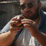 man wearing sunglasses eating hamburger